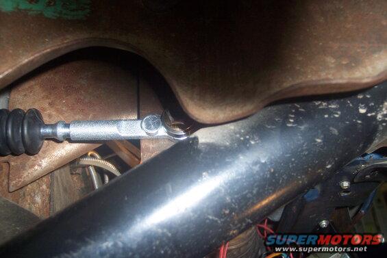 Close-up of a silver steering linkage rod with a black rubber boot, attached to rusty metal components