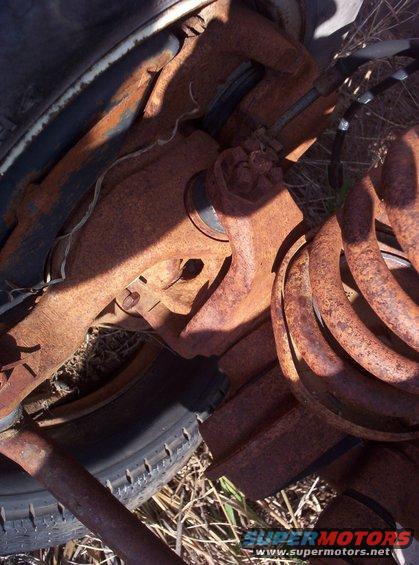 close-up of heavily rusted vehicle suspension components, including a coil spring and part of a tire