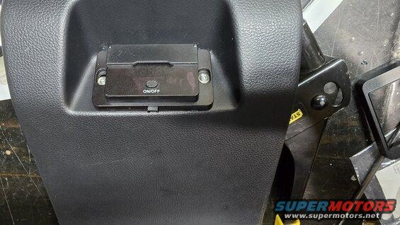 Close-up of a black plastic panel with an OBD-II port cover that has an ON/OFF button