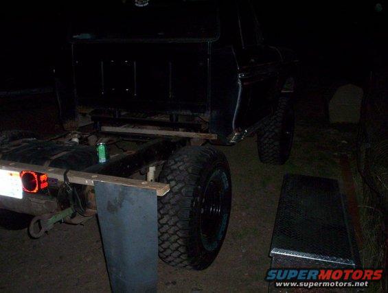 Black truck chassis with large tires, rear view, showing fuel tank and trailer hitch