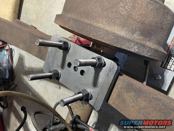 Custom bracket bolted to a rusty beam with a brake drum above