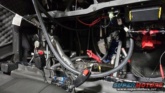 Vehicle interior with complex wiring, battery, and seatbelt buckle visible