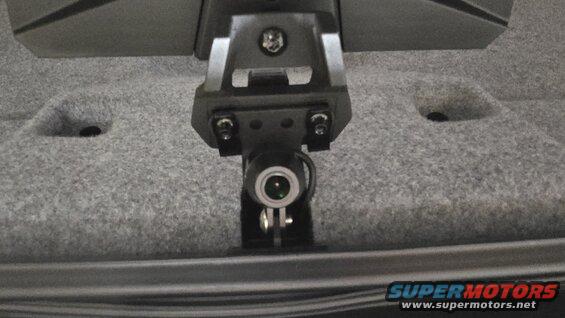 Dash cam mount attached to gray carpeted surface, with a small camera lens visible