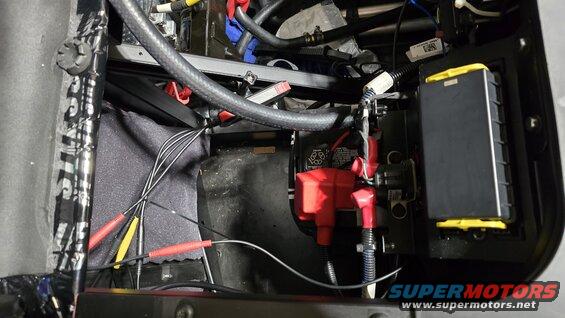 Vehicle battery terminals with red and black covers, wires, and a black fuse box with yellow accents