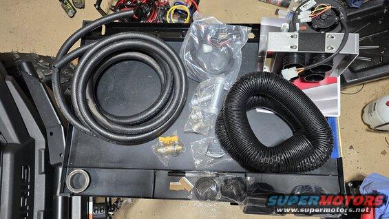 Parts for a vehicle heater kit laid out on a surface, including hoses, a fan unit, and various connectors