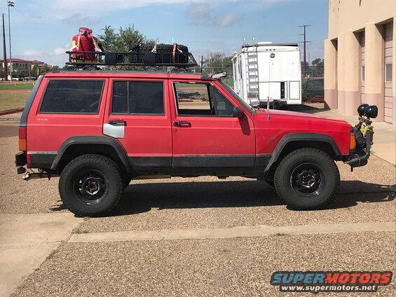 Red 1996 Jeep Cherokee side view with roof rack carrying a red container and spare tire