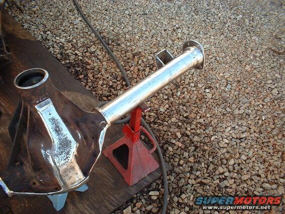 Differential axle assembly on red jack stands, resting on wooden planks and gravel