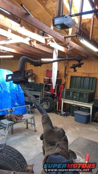 Suspension part held by gloved hand in garage, with tools and storage bins in background