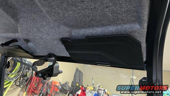Inside of a UTV, showing the gray upholstered roof, black visor panels, and a windshield with items behind it