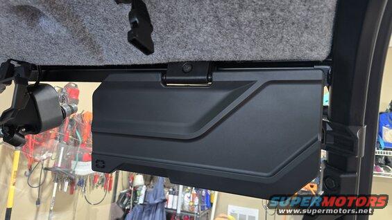 Black plastic storage compartment mounted inside a vehicle, with a gray headliner above