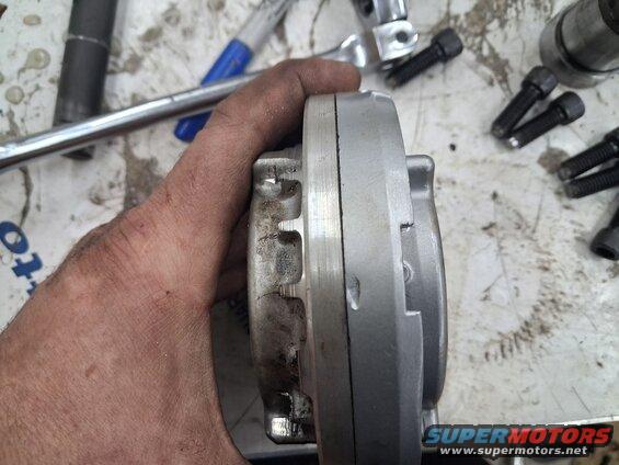 Metal part with gear teeth held by a hand, with tools and bolts scattered on a surface