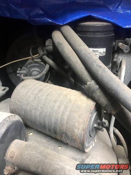 Engine components under a blue tarp with visible hoses and a cylindrical part