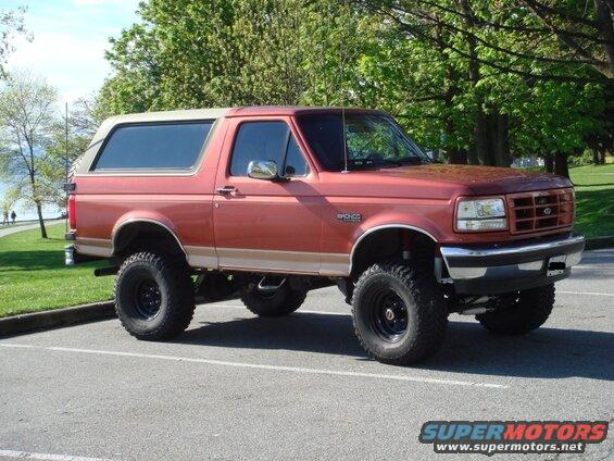 Lifted red and tan Ford Bronco SUV with off-road tires parked in a lot.