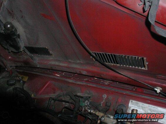 Underside of a red vehicle hood with vents and engine components visible.