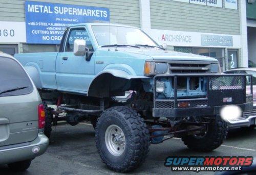 Lifted light blue pickup truck with large off-road tires and a custom bumper.