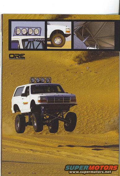 White lifted Ford Bronco jumping over sand dunes with a light bar on the roof.