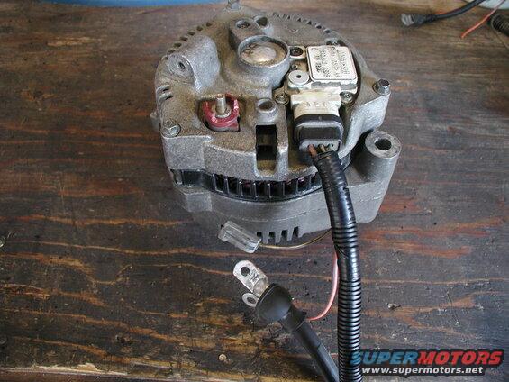 Vehicle alternator with wiring harness and battery cable on a wooden surface.