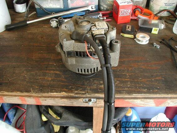 Car alternator on a workbench with tools and supplies.