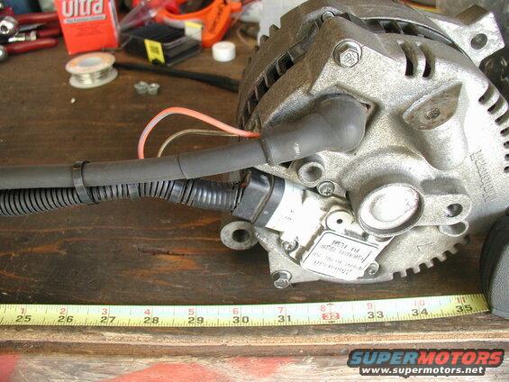 Rebuilt Motorcraft alternator with wiring harness on a wooden surface with tape measure.