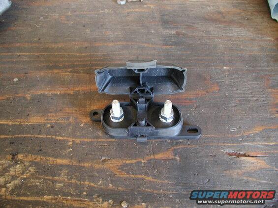 Black plastic automotive part with two bolts on a wooden surface