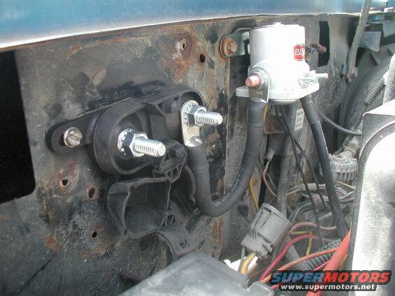 Close-up of electrical components in engine bay: solenoid, wiring, bracket.