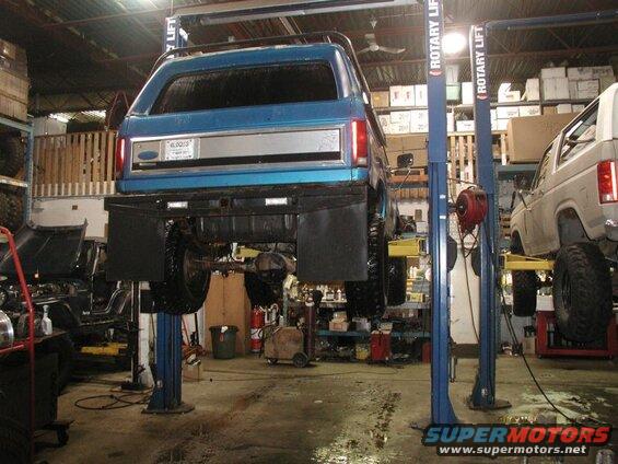 Rear view of a blue Ford Bronco on a car lift in a garage.