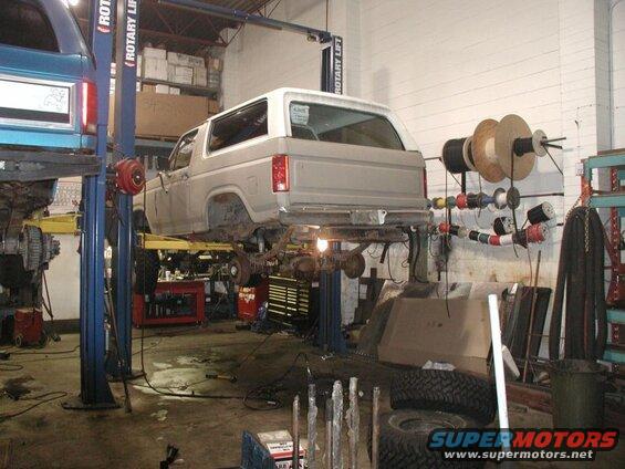 Light-colored SUV on a lift in a garage, with another blue SUV on a lift to the left.