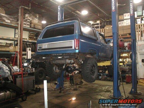Blue 1985 Ford Bronco on a car lift in a garage, rear view.