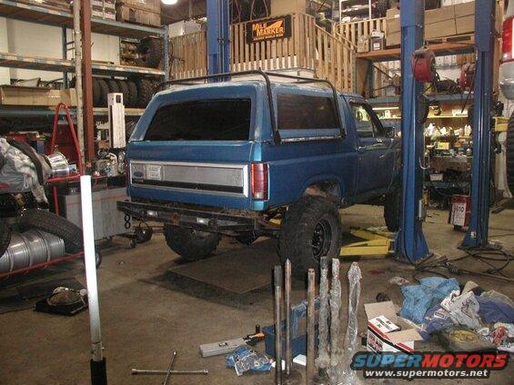 Blue Ford Bronco on a lift in a garage with metal shafts on the floor.