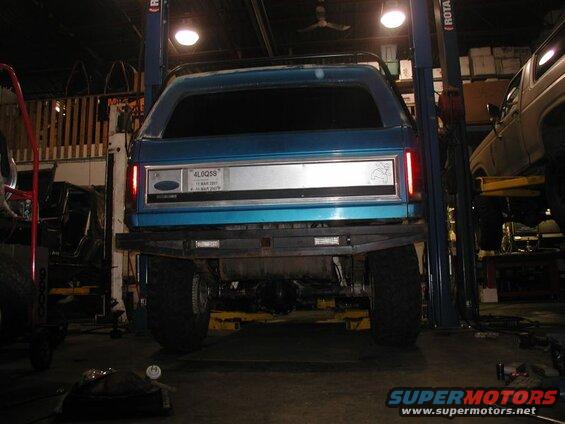 Rear view of a blue Ford Bronco on a car lift with custom bumper and large tires.