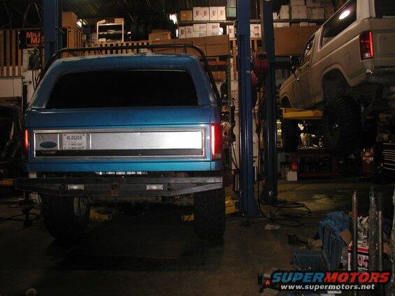 Rear view of a blue Ford Bronco in a garage, lifted on a car lift.