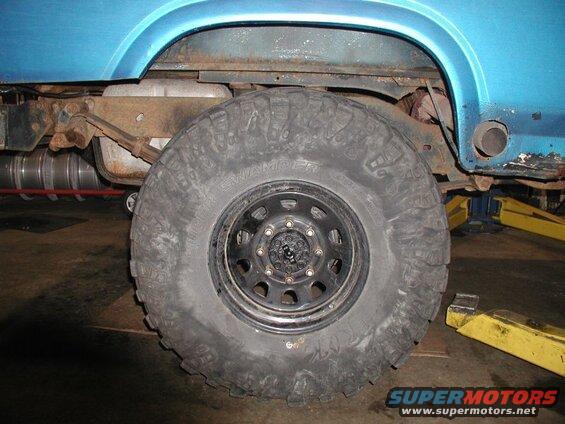 Rear wheel and suspension of a blue Ford Bronco with off-road tires on a lift.