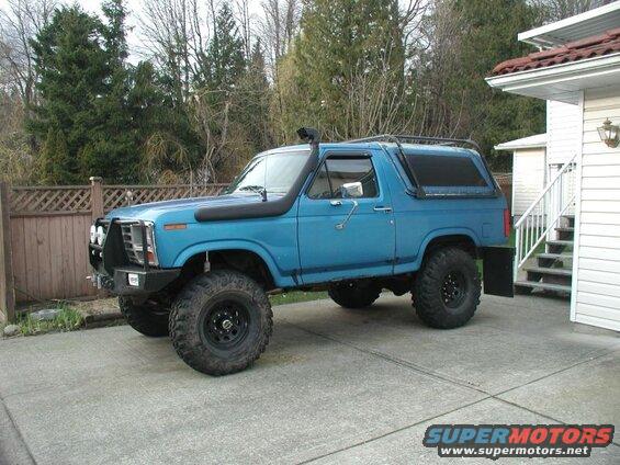 Blue lifted Ford Bronco with snorkel and roof rack parked on driveway.