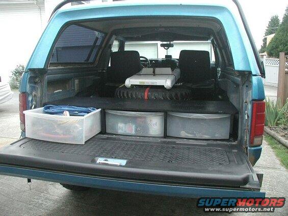 Teal Ford Bronco tailgate down, showing storage platform with bins and spare tire.