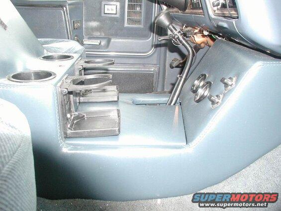 Custom center console with cup holders, gear shifter, and switches inside a vehicle.