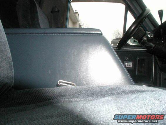 Interior of a vehicle showing blue upholstered seat and console with chrome seatbelt buckle.