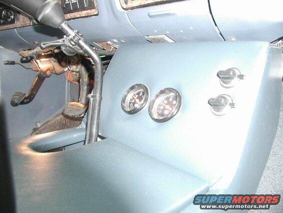 Vehicle interior with gauges, knobs, steering column, and pedals.