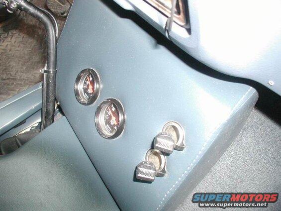 Close-up of a vehicle's grey upholstered dashboard with two gauges and three toggle switches.