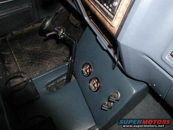 Interior of a blue 1985 Ford Bronco with floor shifter, two gauges, and keys in the ignition.