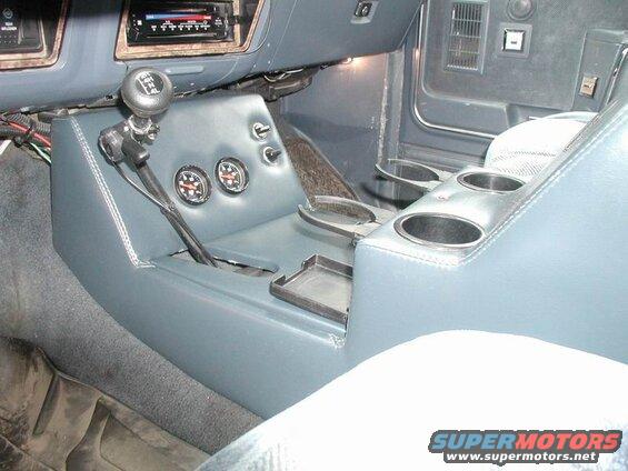 Interior of a vehicle showing a custom center console with shifter, gauges, cup holders, and aftermarket radio.