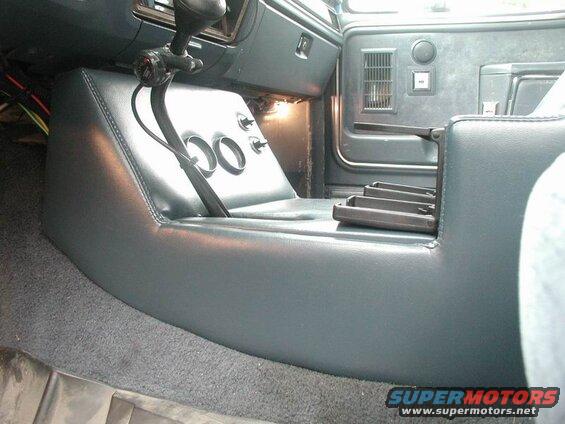 Vehicle interior showing custom center console with gear shifter, gauges, and fold-out tray.