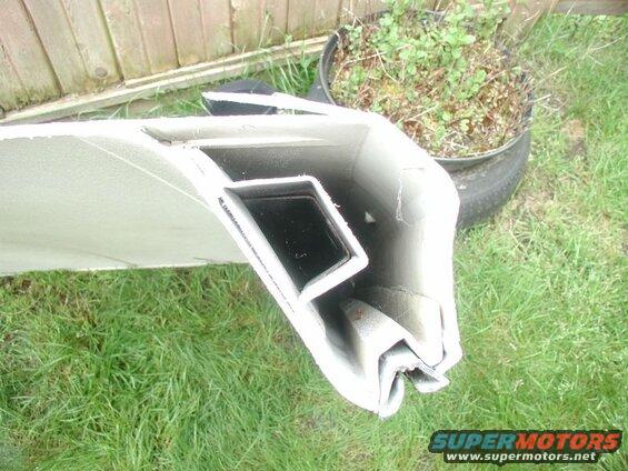 Damaged light-colored structural part with black interior channel on grass.