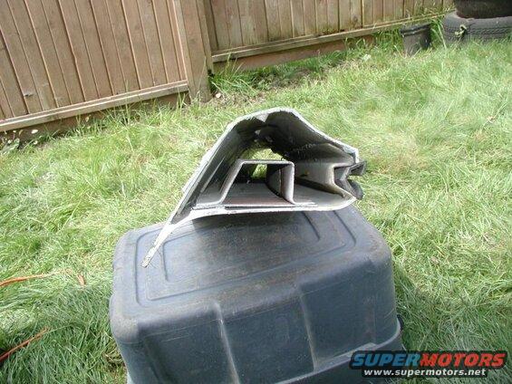 Damaged silver and black metal car part on a black plastic bin