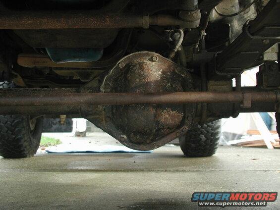 Underside of a vehicle showing a rusty differential, leaf springs, and off-road tires.