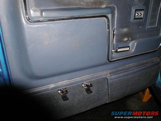 Interior door panel of a blue vehicle with gray panel and carpeted lower section with clips.