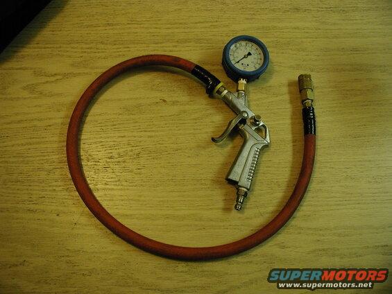 Tire inflator gun with pressure gauge and red hose on a wooden surface.