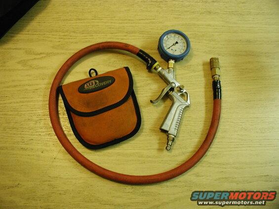 Tire inflator with gauge and orange storage pouch on a wooden table.