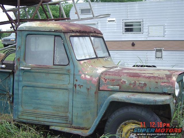 Side view of a rusty 1947 Willys pickup truck cab, painted teal and red, with a trailer behind it