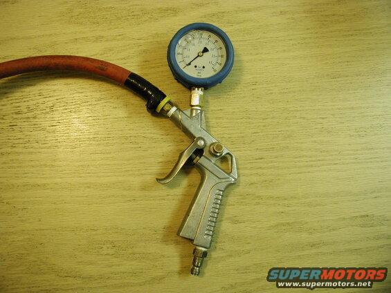 Air compressor blow gun with pressure gauge and red hose on a wooden surface.