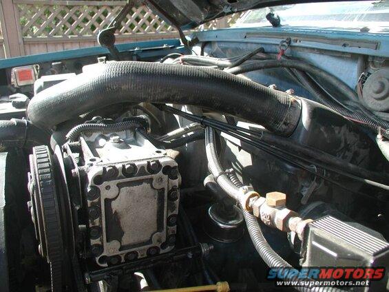 Engine bay of a blue Ford Bronco, showing AC compressor, hoses, and wiring.